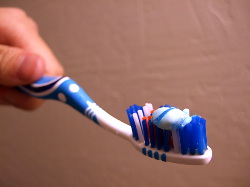 A hand applies white and blue toothpaste to a toothbrush, relating to careers in film.